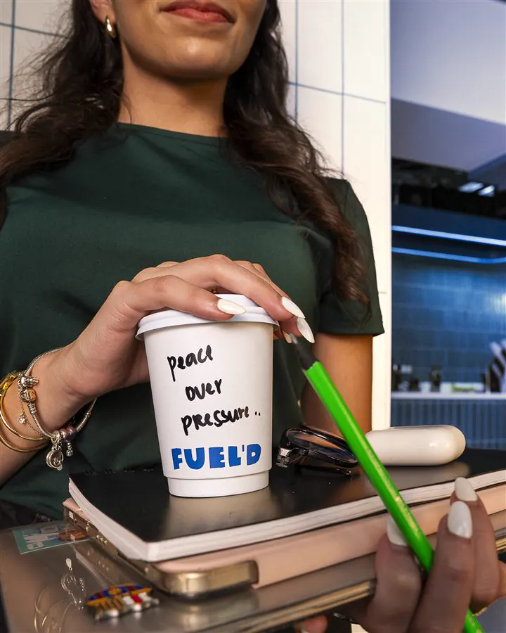 A Fuel'd cup with 'peace over pressure' handwritten on it, on a stack of notebooks