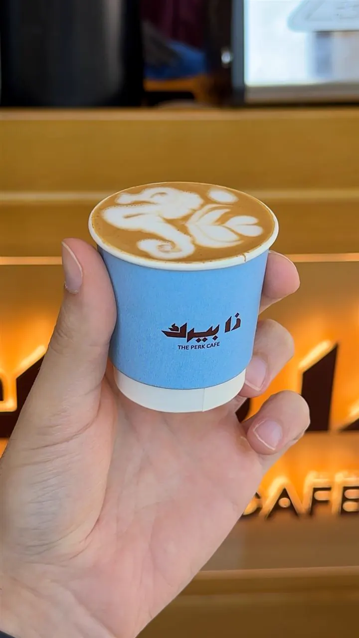 The Perk Cafe: a cortado held in front of the sign
